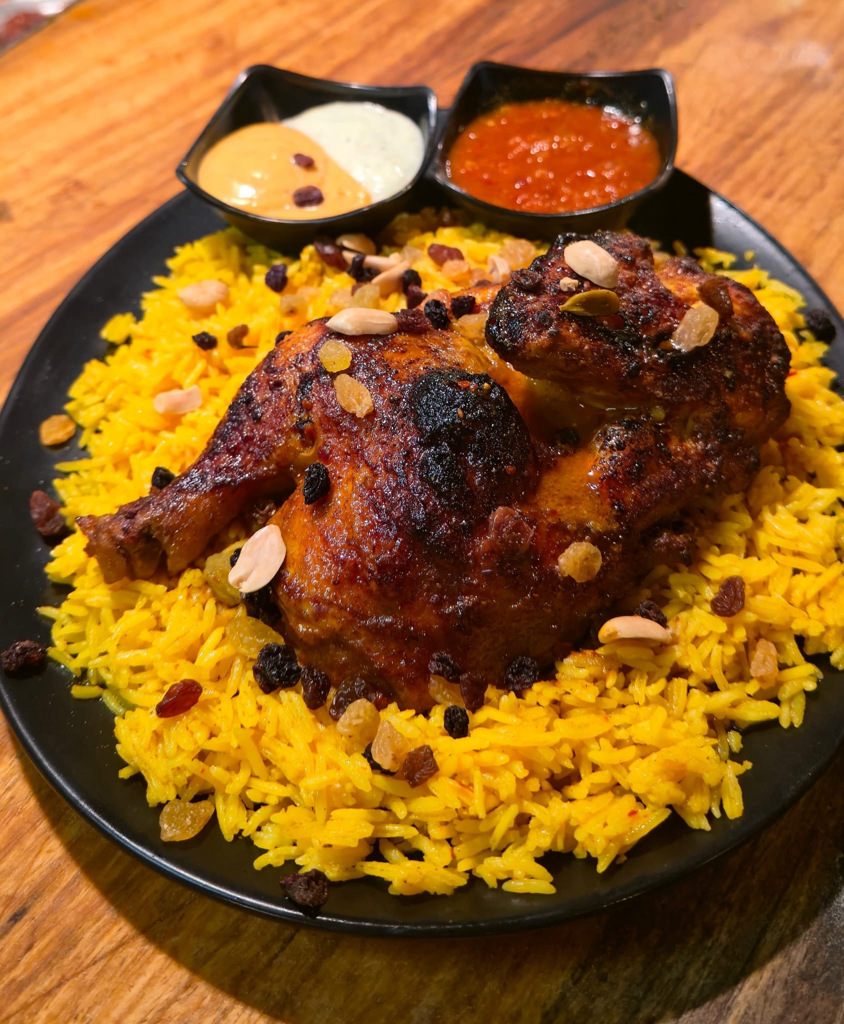 Mandi Poulet ( cuisson lente d'un demi poulet marinés aux épices douces, servi sur un lit de riz basmati parfumé, agrémenté de raisins secs et cacahuètes croquantes)